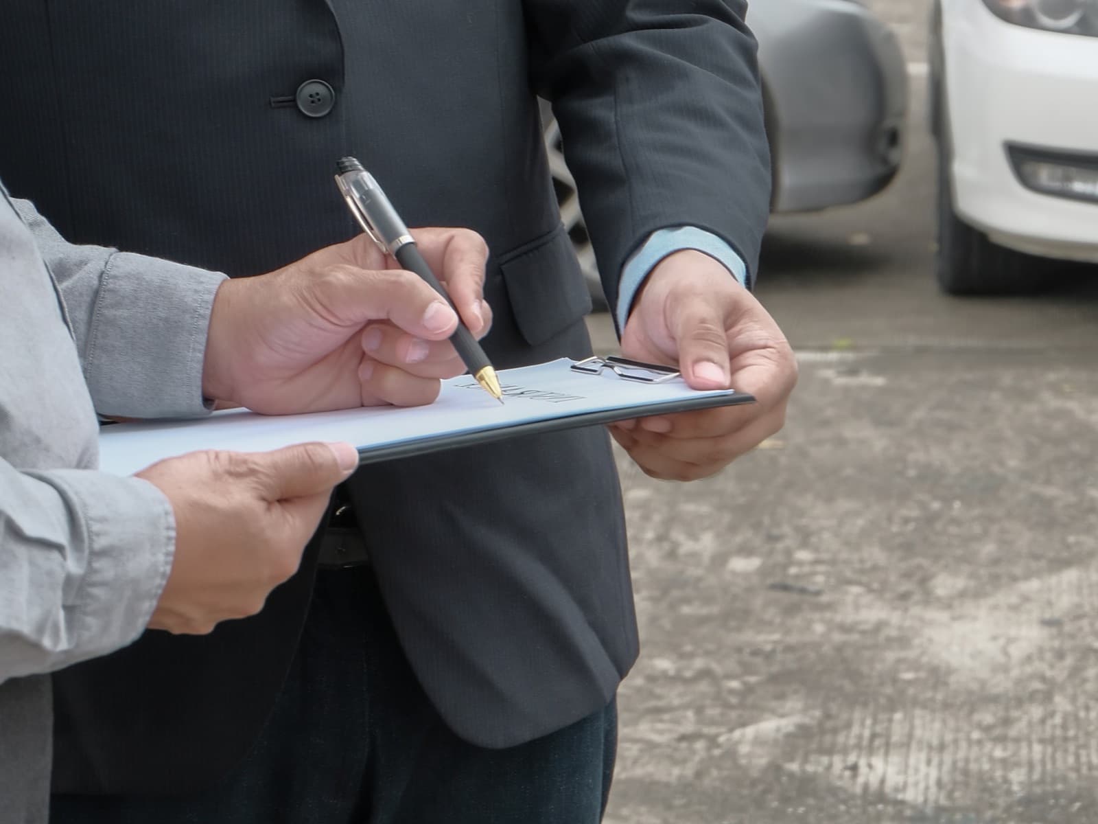 Men signing on clipboard near parked cars.