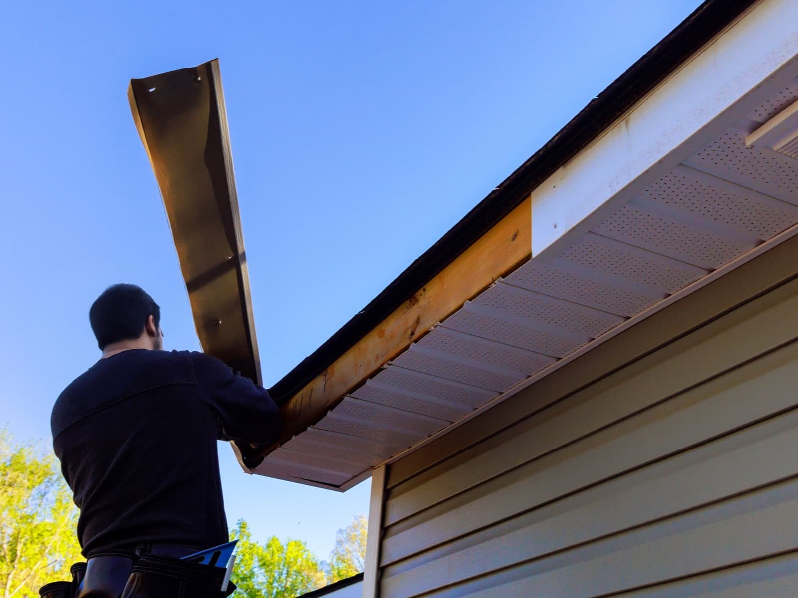 Man repairing soffit under blue sky.