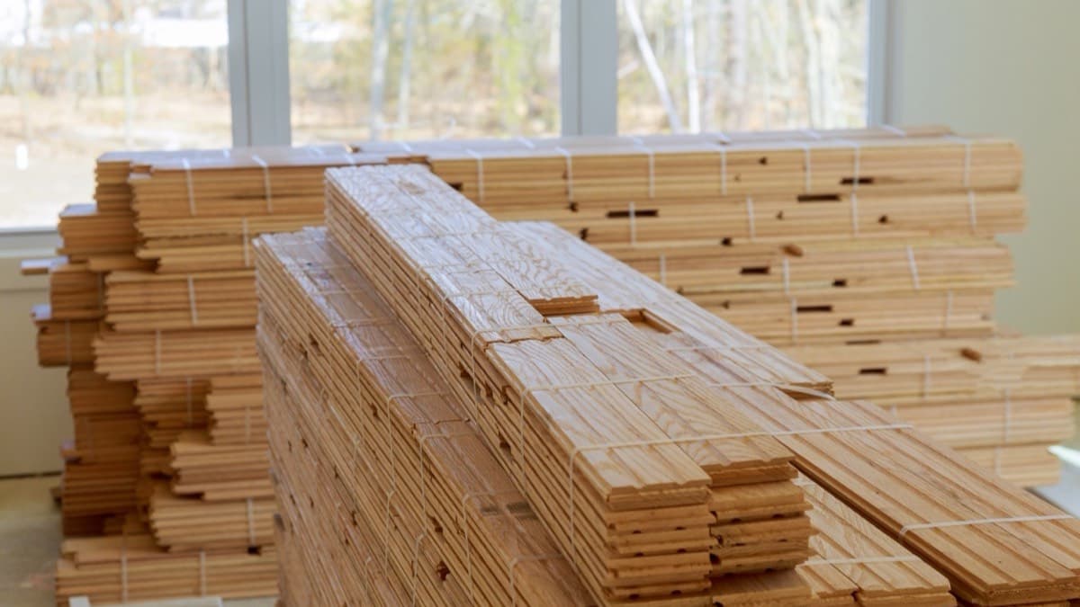 Bundles of new wood flooring stacked in a sunlit room before installation