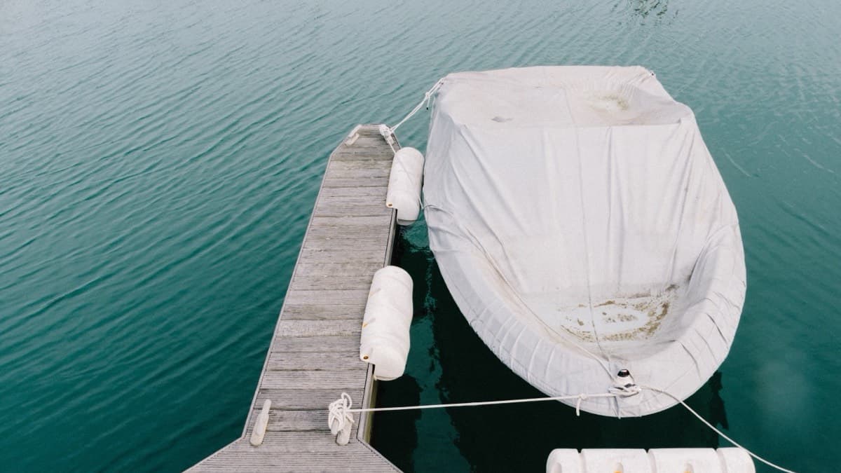 A small boat under a fitted white cover, tied up beside a wooden dock in calm green water