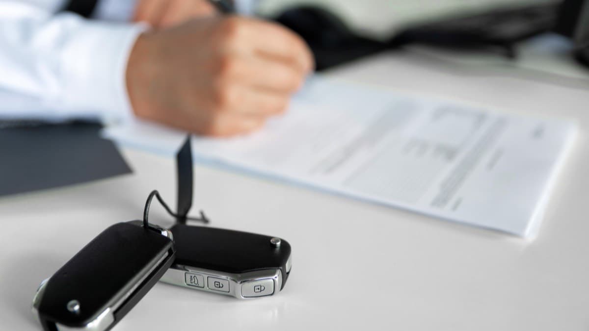 A person signing a contract at a white desk with a car key fob in the foreground