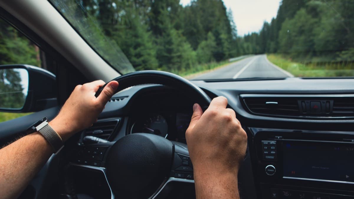 A driver with both hands on the steering wheel on a forest road