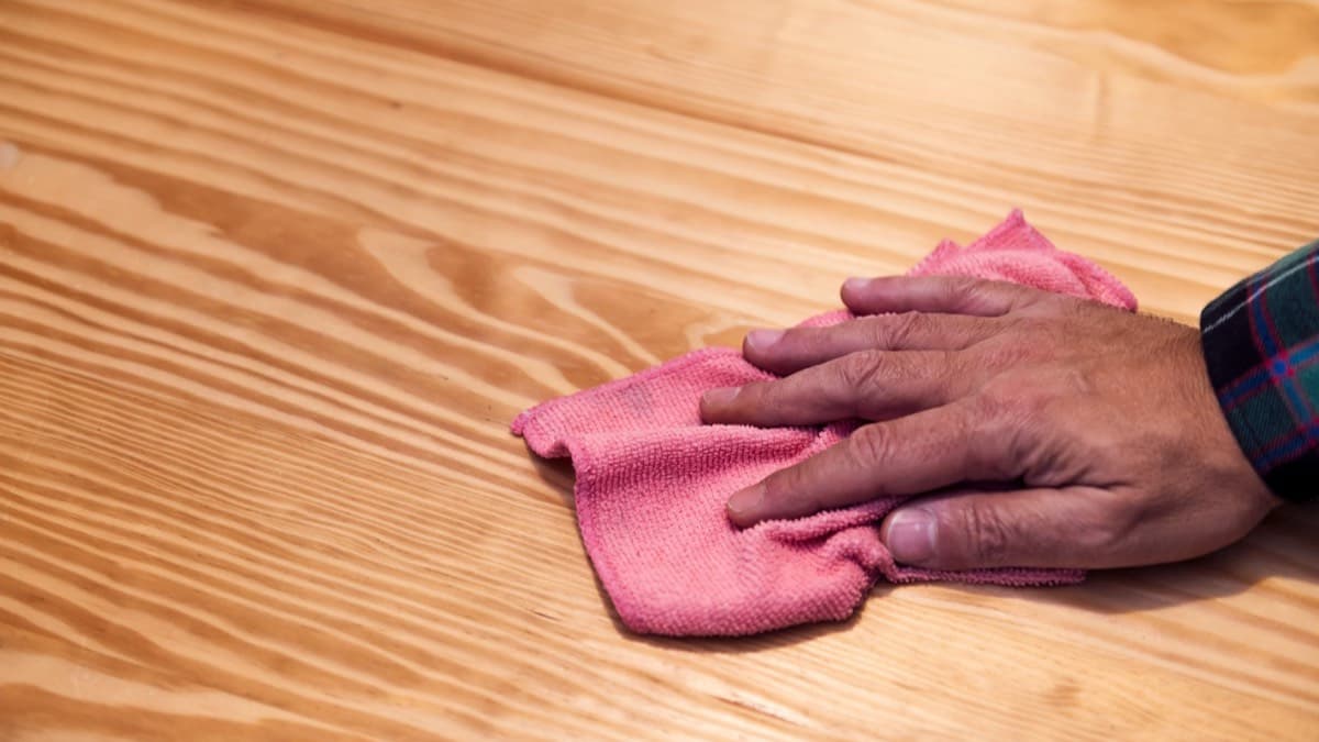 A hand wiping a wooden tabletop with a soft cloth