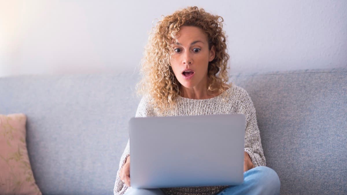 A surprised woman looking at a laptop on her sofa