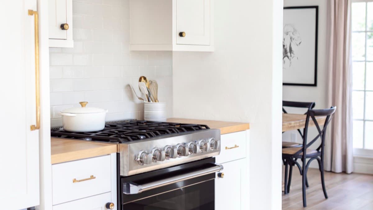 A freestanding stainless steel range between white cabinets in a bright kitchen