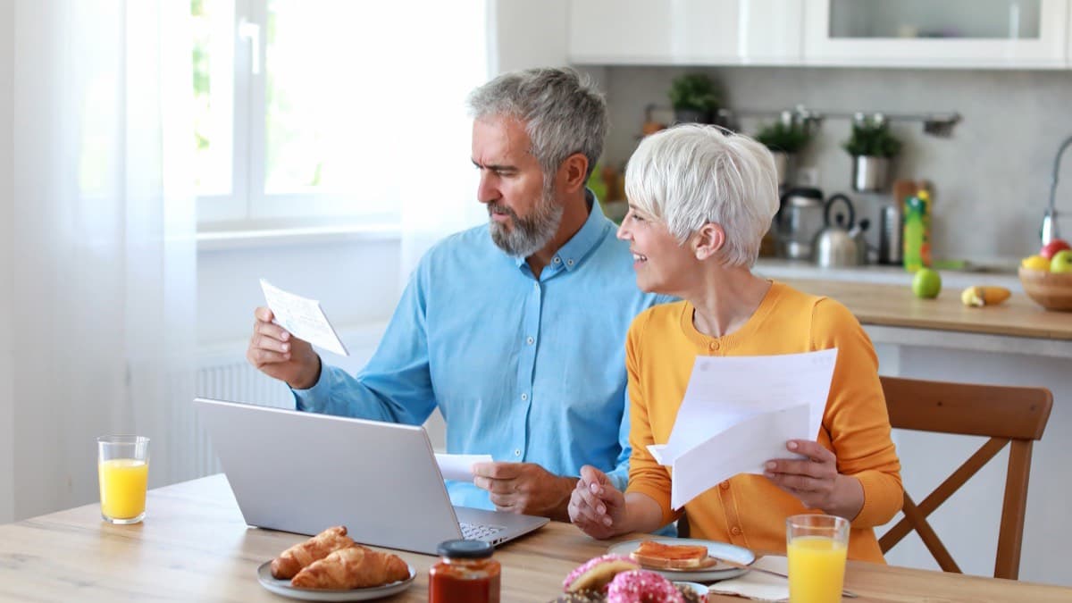 An older couple reviewing papers and a laptop at their kitchen table