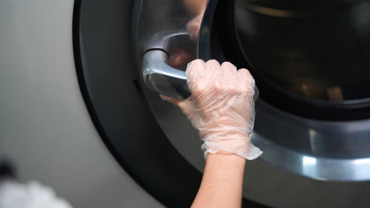 A gloved hand opening the door of a front-load washer