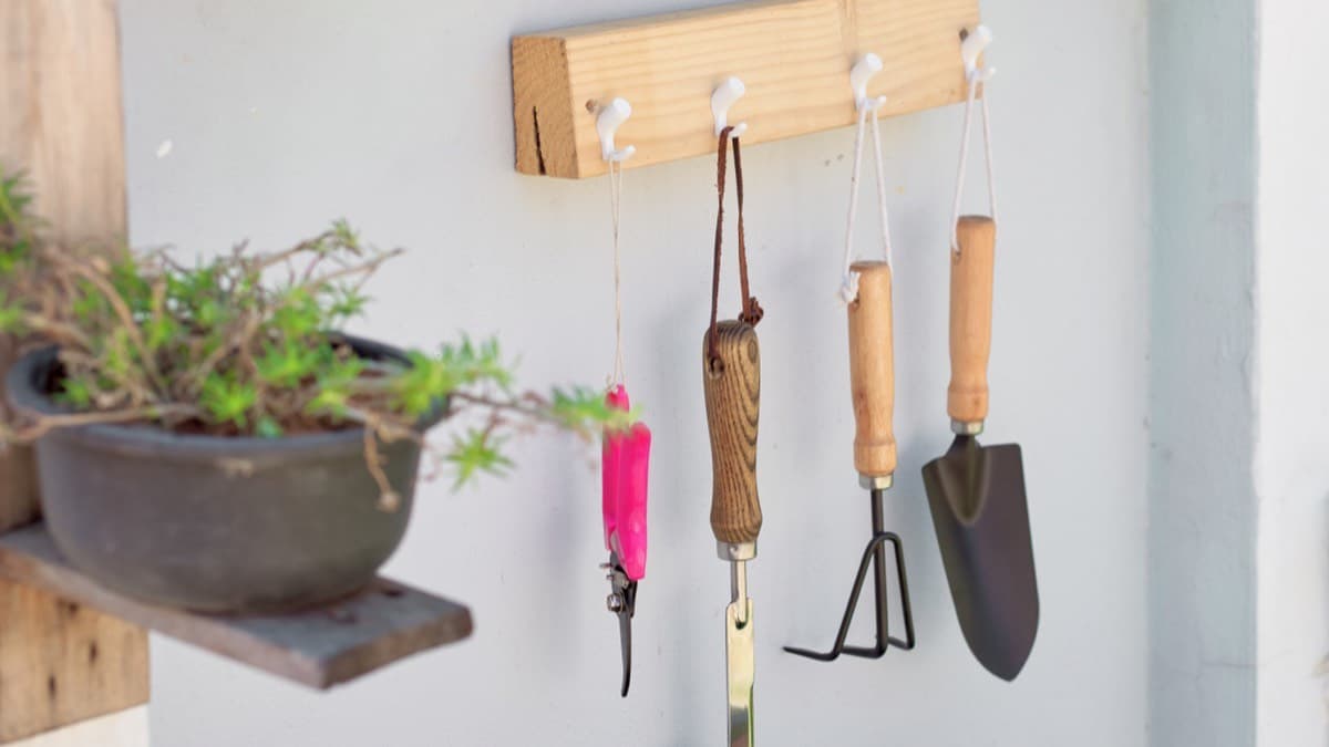 Hand garden tools hanging from wooden hooks on a white wall