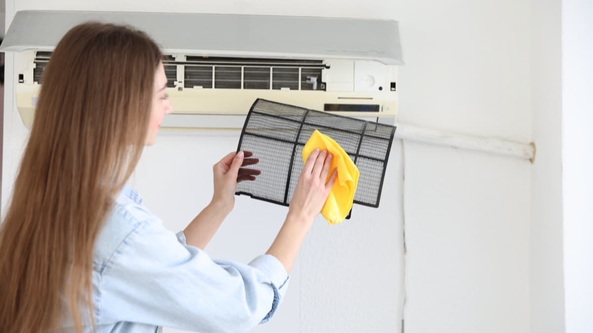 A woman wiping a mesh filter taken from a wall-mounted air conditioner