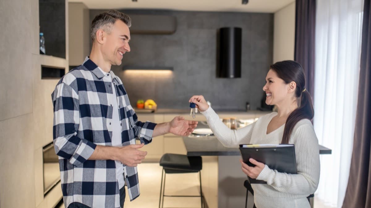 A woman holding a folder handing keys to a man in a finished modern kitchen