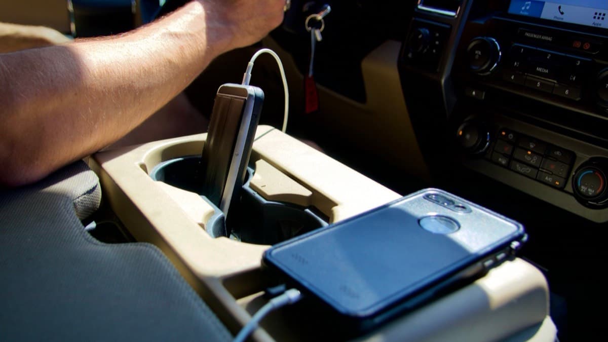 A phone lying face down on a car's center console while the driver keeps a hand on the wheel