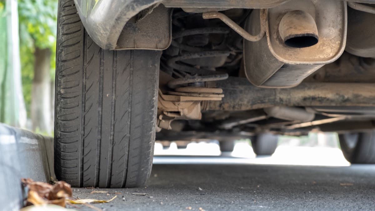 A low view of a parked car's underside, exhaust and rear tire above the pavement