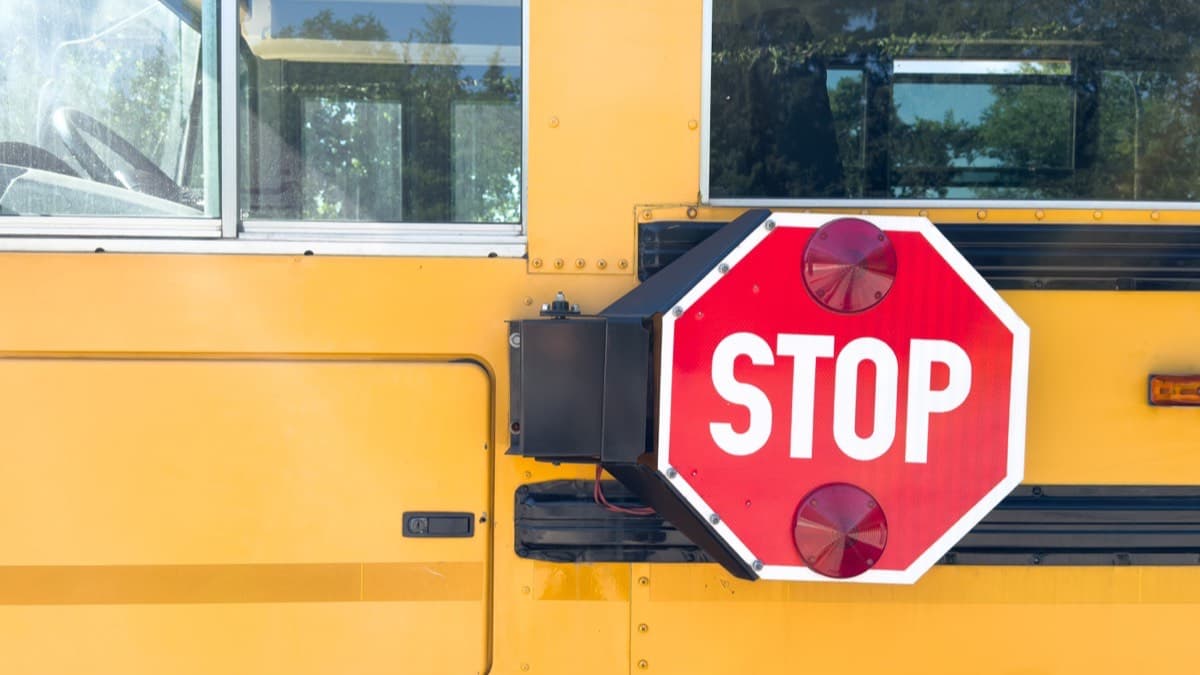 The red stop arm and warning lights on the side of a yellow school bus