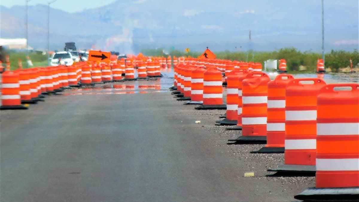 Rows of orange and white barrels channeling a road through a work zone, with traffic beyond