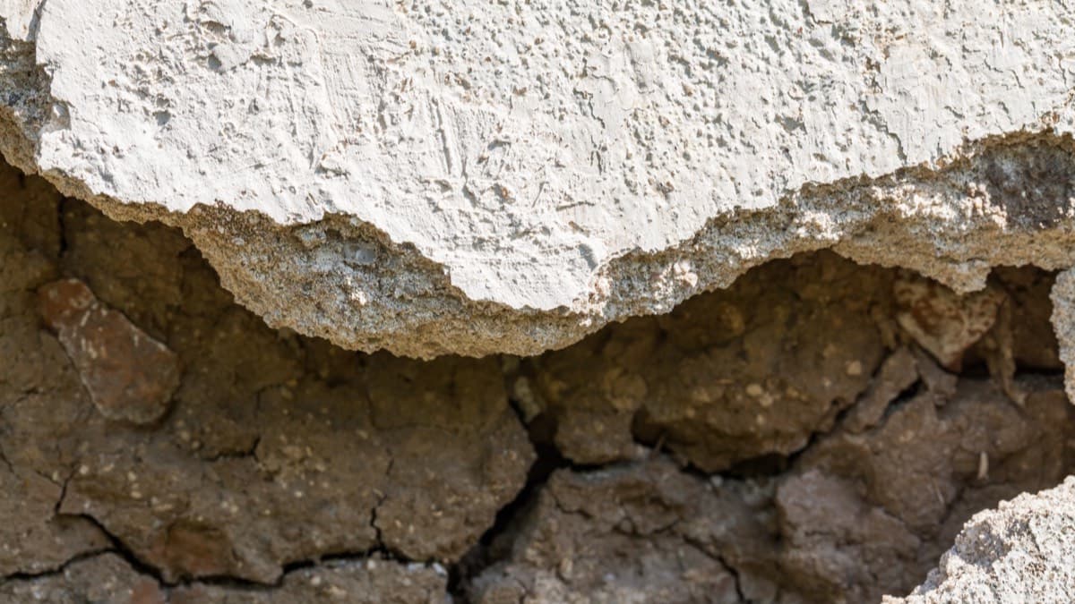 Dry clay soil shrunk and cracked beneath the edge of a concrete slab