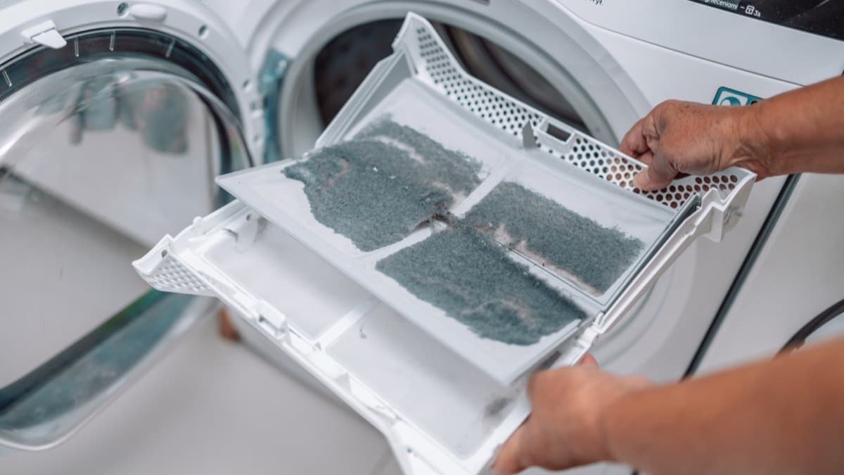 Hands pulling a lint-caked filter out of a clothes dryer