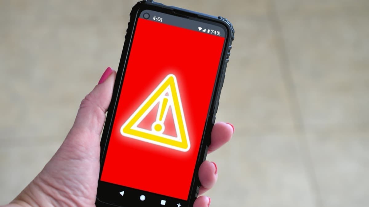 A hand holding a smartphone whose screen shows a yellow warning triangle on a red background