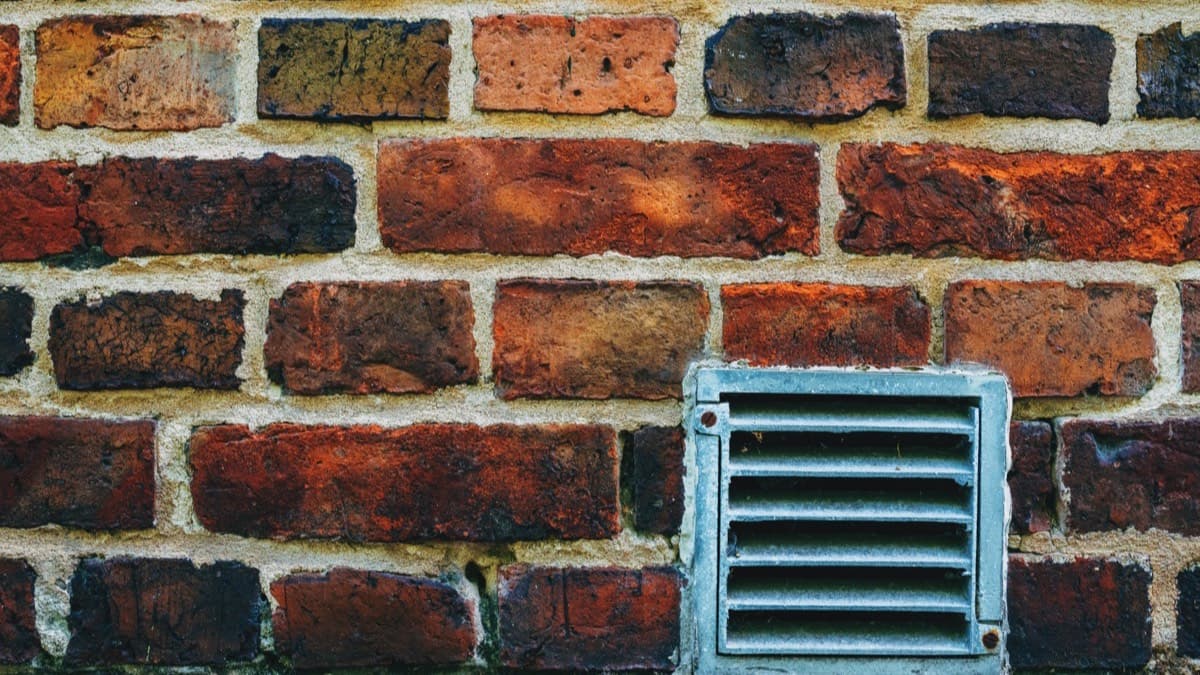 A louvered metal vent set low in an old brick wall just above the ground