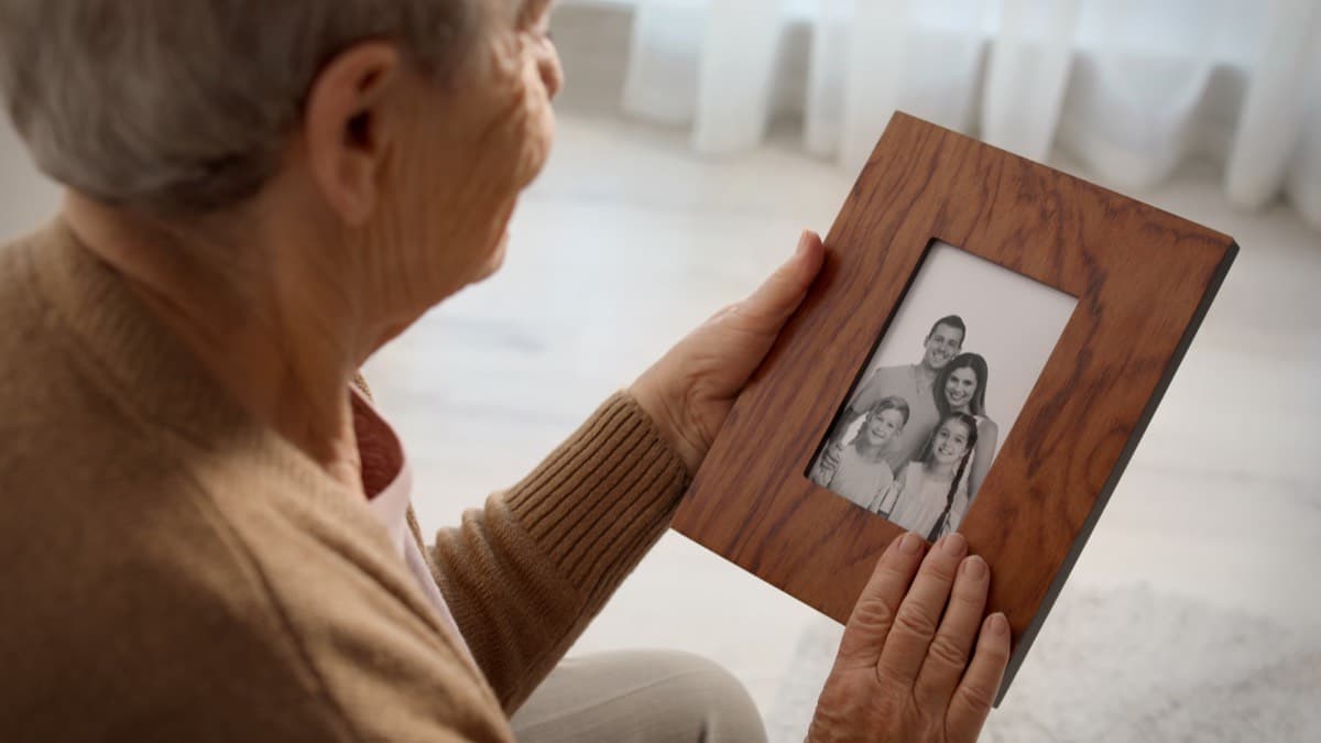 An older woman holding a wooden frame with a black and white family photograph in it