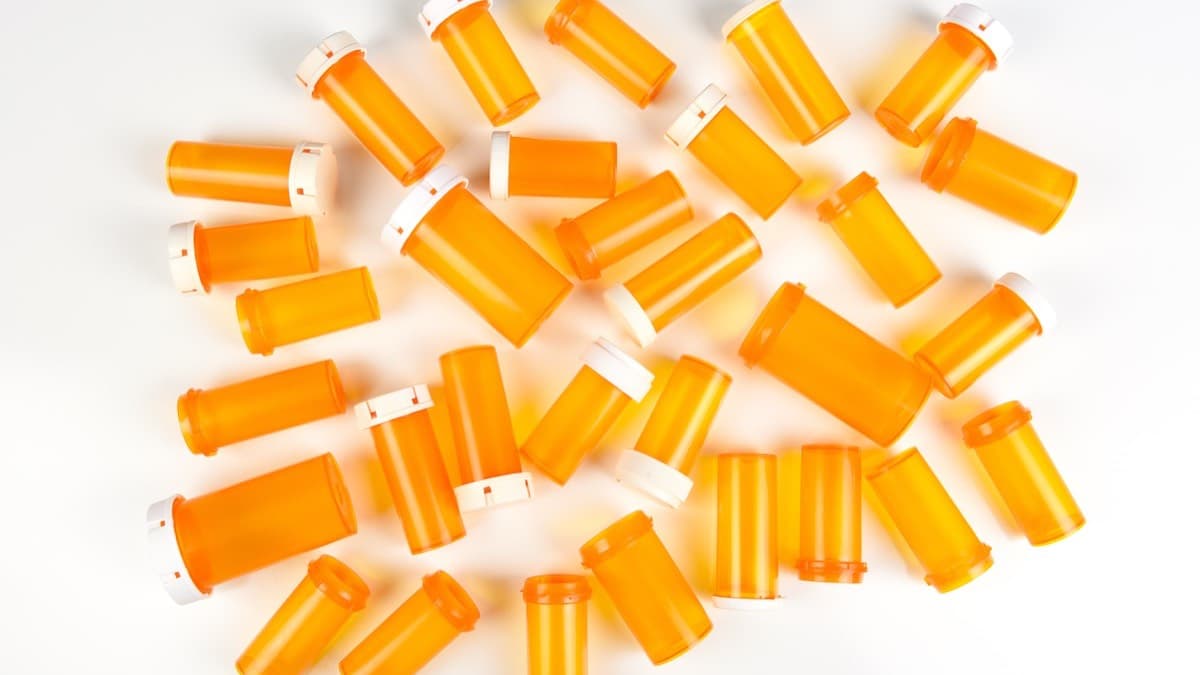 Dozens of empty orange prescription pill bottles with white caps scattered on a white surface