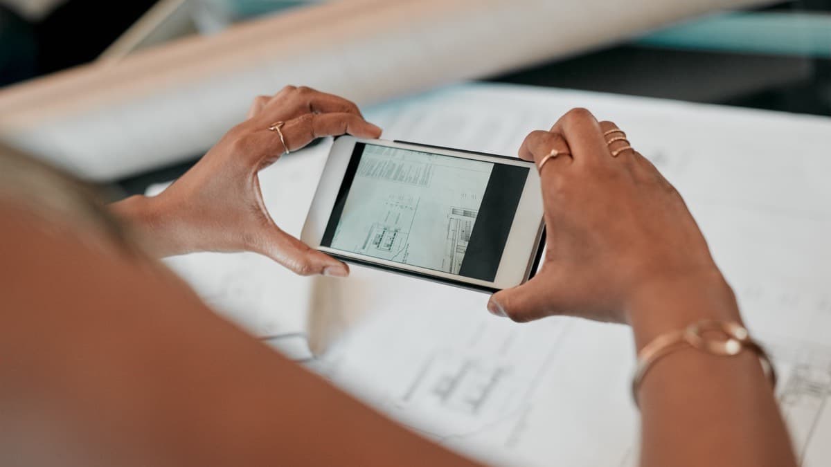 Hands holding a phone sideways to photograph printed papers spread on a table