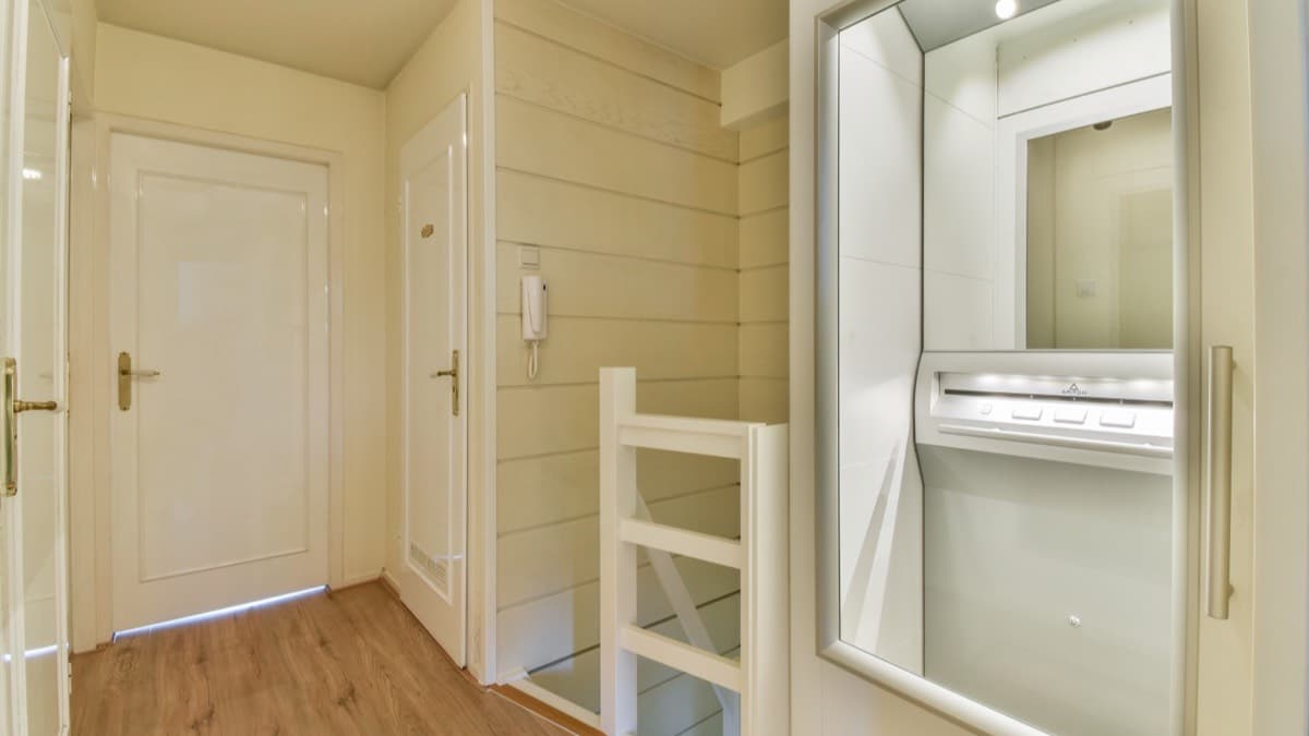 A small home elevator cab set into the wall of an upstairs landing, beside the stair rail and two bedroom doors