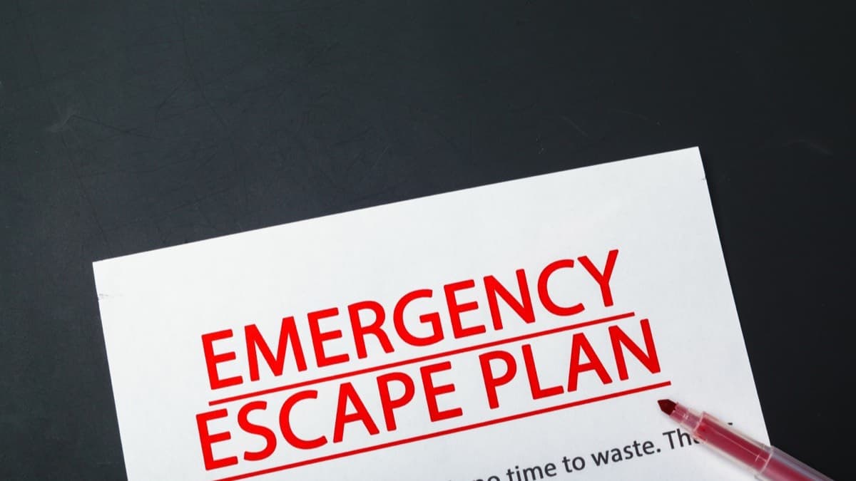 A white sheet headed EMERGENCY ESCAPE PLAN in red capitals lying on a dark surface, a red marker resting on it