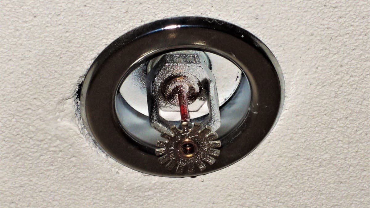 Close-up of a chrome fire sprinkler head with a red glass bulb, recessed in a white textured ceiling