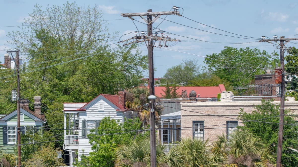 Wooden utility poles with transformers carrying power lines over the rooftops of older clapboard houses