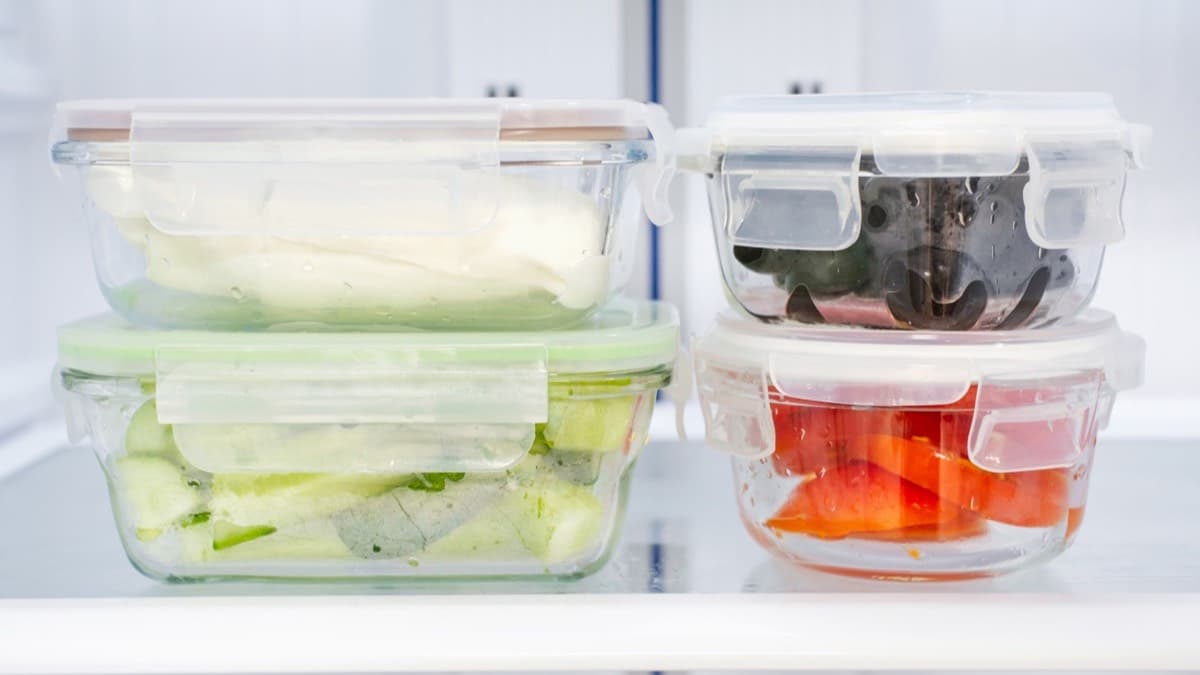 Four glass storage containers of prepared food stacked in pairs on a refrigerator shelf