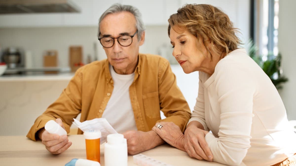 An older couple at a kitchen table reading the labels on prescription bottles