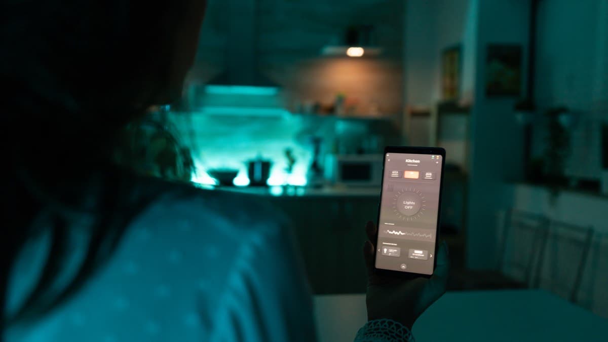 A hand holding a phone open to a lighting app in a dim kitchen