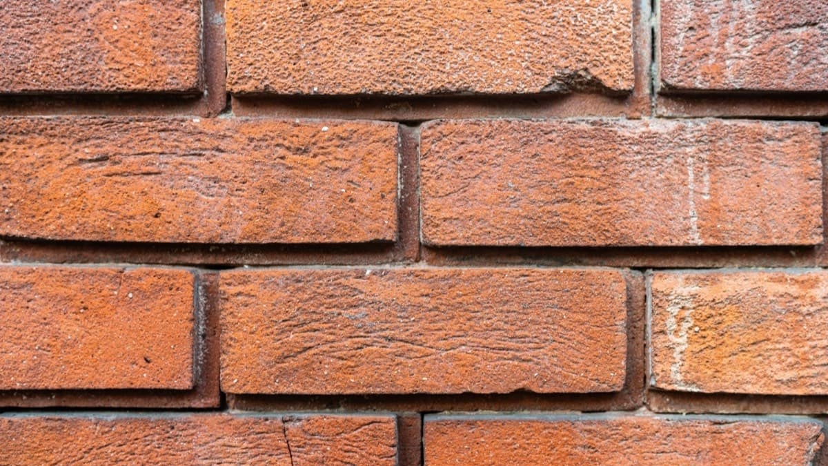 A weathered red brick wall with worn, recessed mortar joints