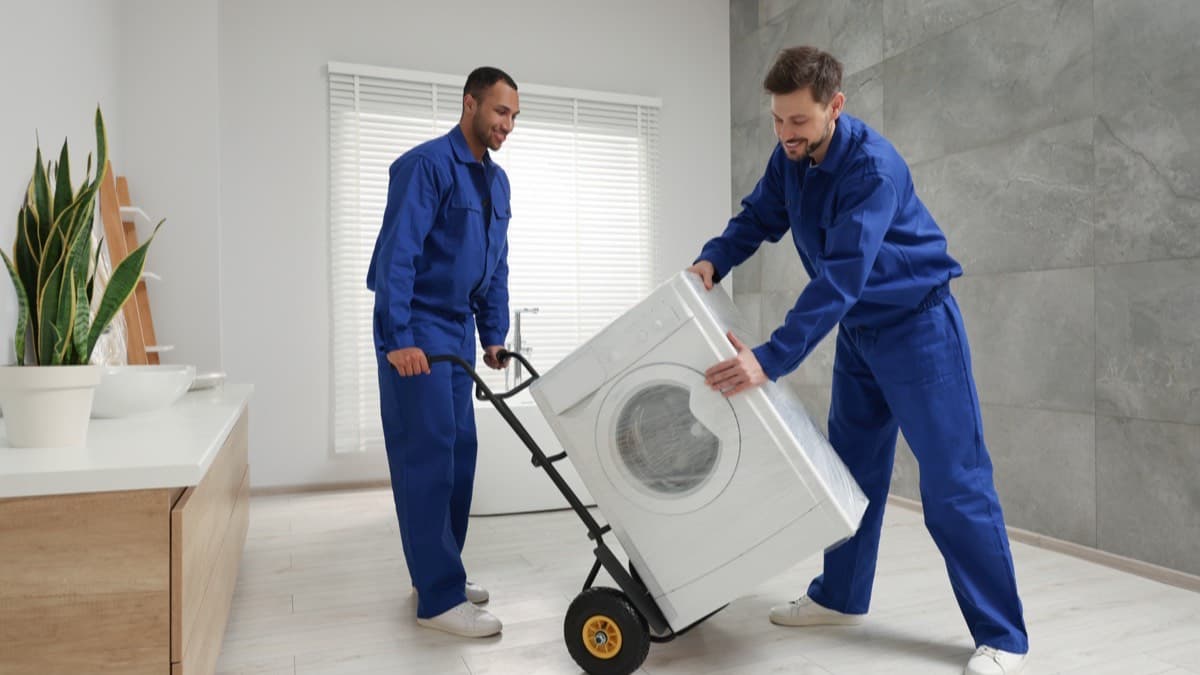 Two movers wheeling a front-load washing machine on an appliance dolly