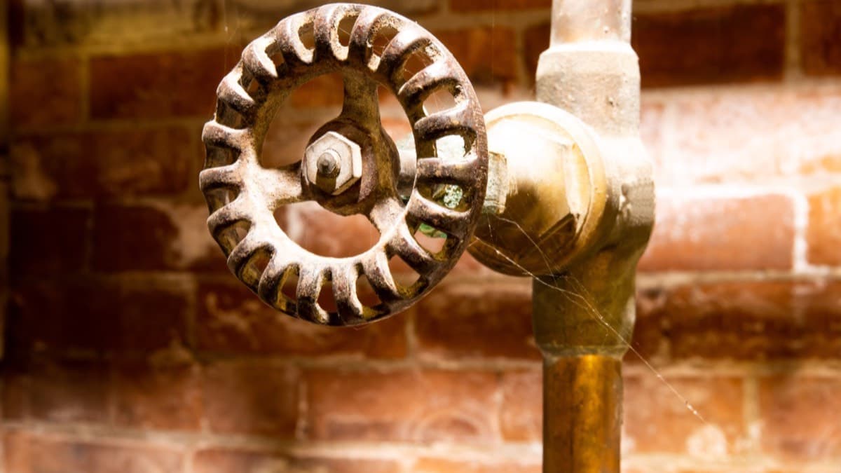 A brass wheel-handle water shutoff valve on a pipe against a brick wall
