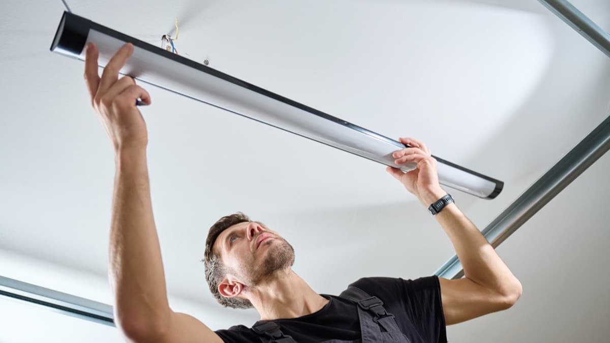A man taking down a long tube light fixture from a ceiling