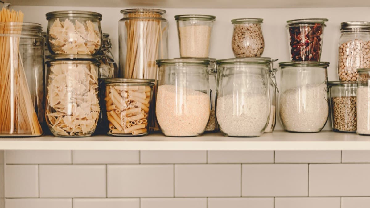 Sealed glass jars of pasta, rice, flour and beans on a pantry shelf