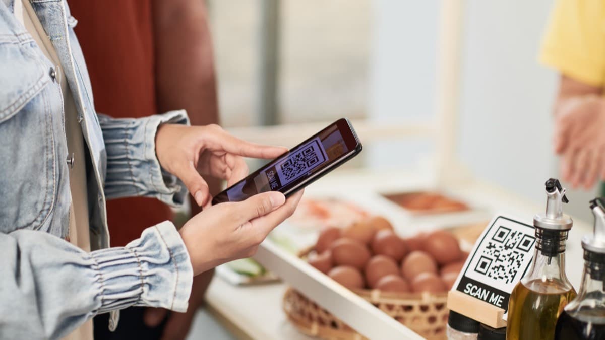 A shopper holding a phone with a QR code up to a market stall's scan-to-pay sign