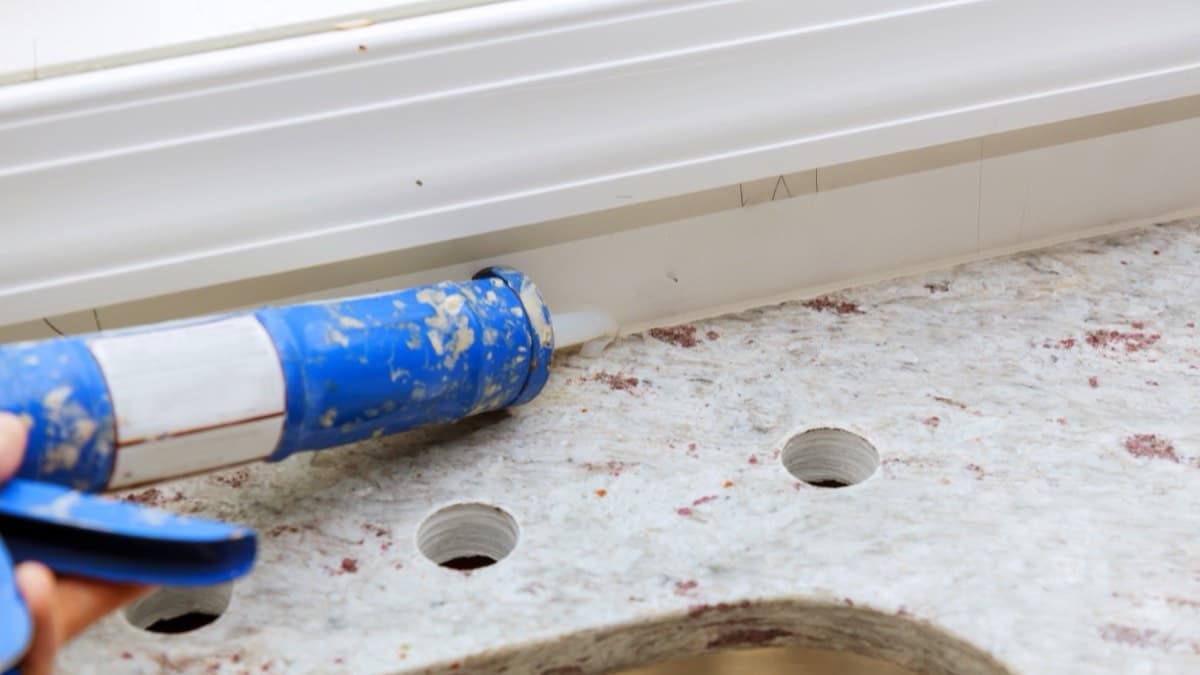 A caulk gun sealing the gap where a stone countertop meets the backsplash