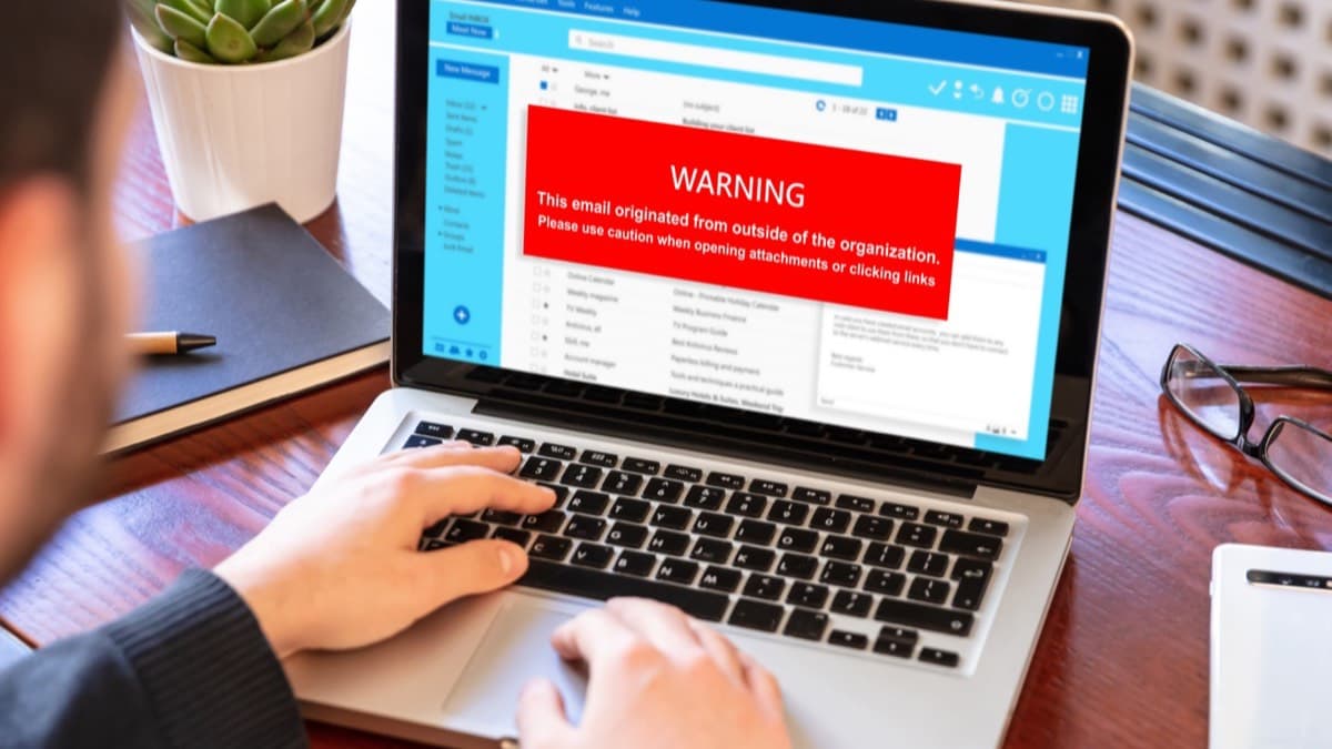 A person typing on a laptop whose email inbox shows a red warning banner over a suspicious message