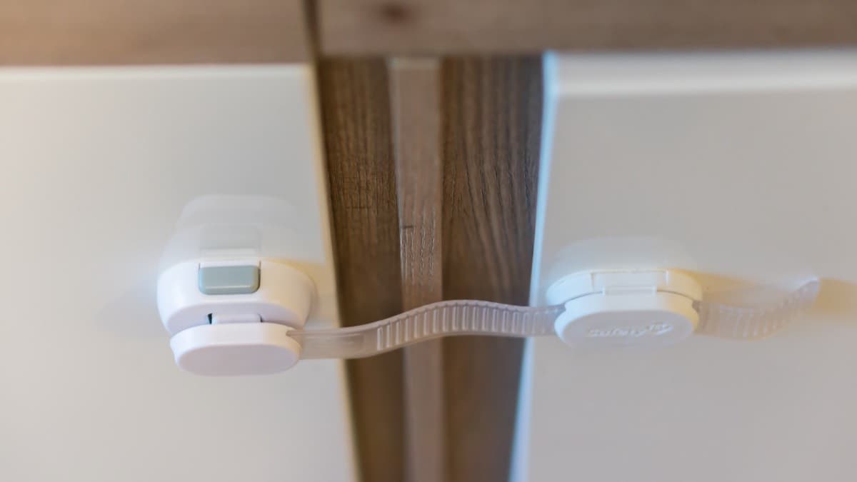 A white child safety strap lock fastened across two cabinet doors