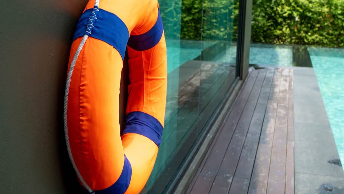 An orange life ring hanging on a wall beside a swimming pool deck