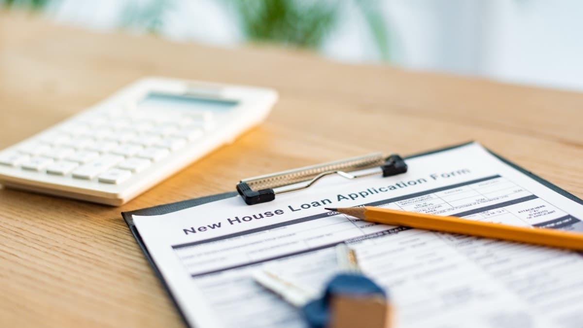 A home loan application form on a clipboard beside a calculator, a pencil and house keys
