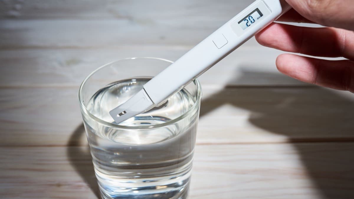 A hand dipping a digital water tester into a glass of water