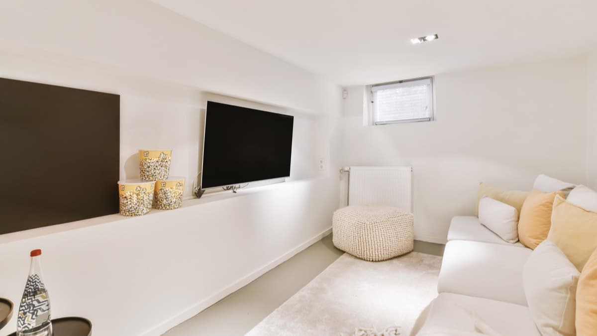 A basement apartment living room with a white sofa and a small window high on the wall
