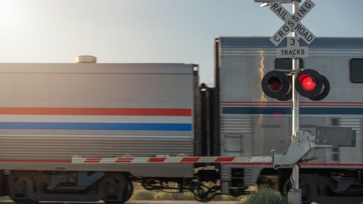 A passenger train passing a railroad crossing with the gate down and the red signal lit