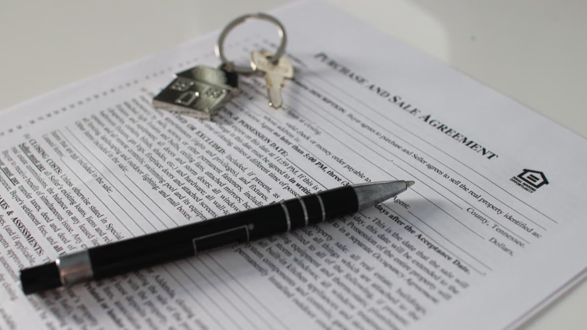 House keys and a pen resting on a printed home purchase agreement