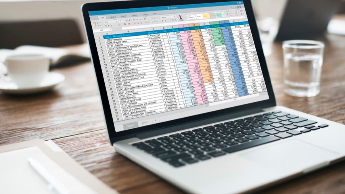 A laptop showing a spreadsheet of monthly figures on a wooden table