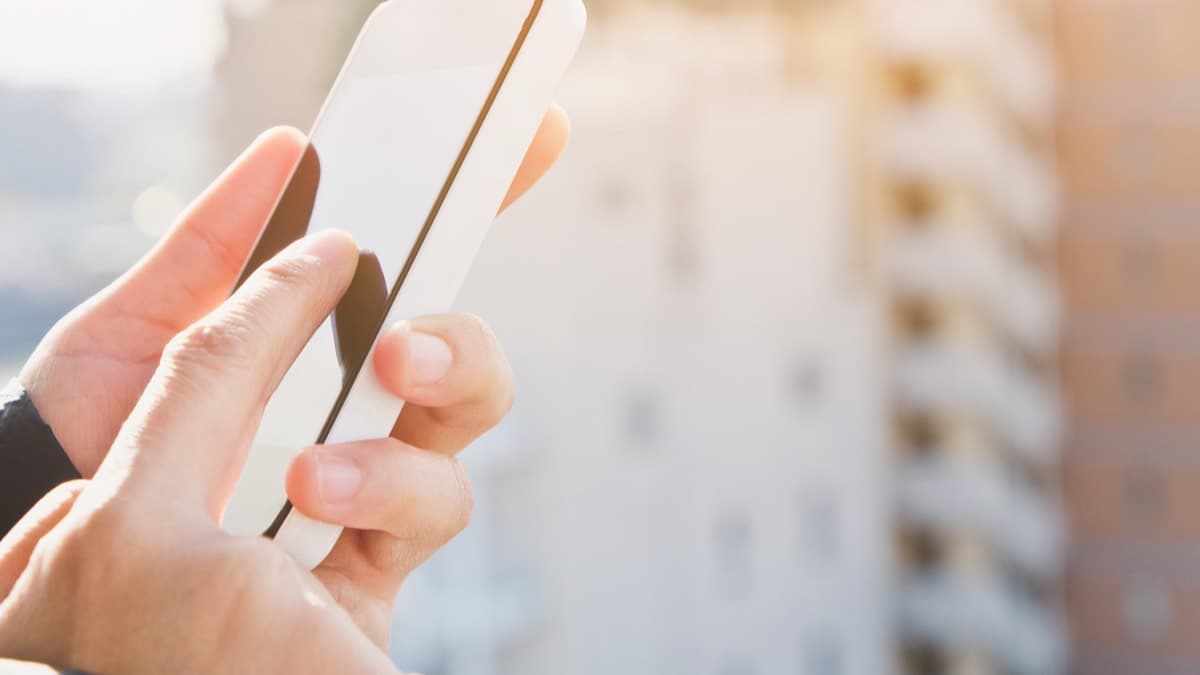 Hands holding a phone in front of a blurred apartment building