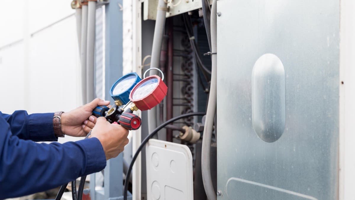 An HVAC technician checking an air conditioning unit with refrigerant gauges